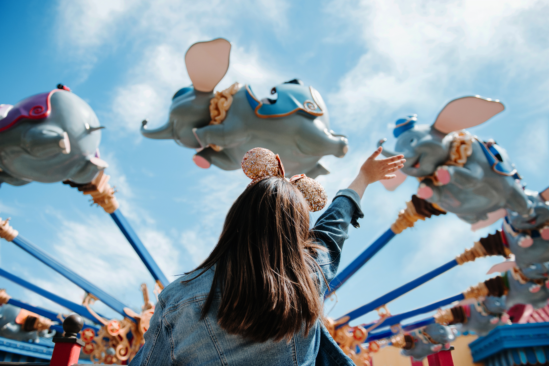 Guest with Minnie ears reaching toward the Dumbo the Flying Elephant ride at Walt Disney World