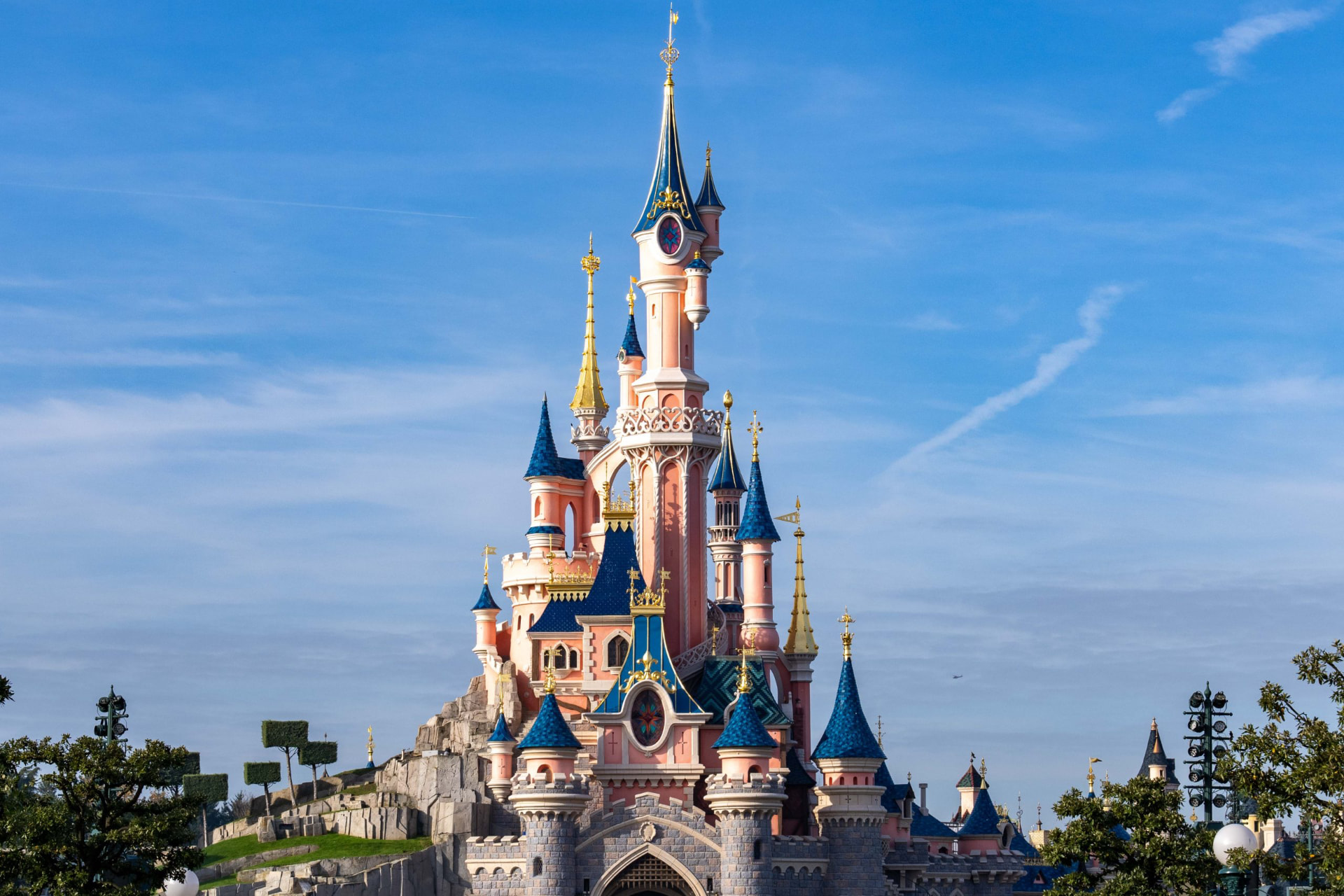 The pink and blue Sleeping Beauty Castle at Disneyland Paris rising above its hill against a clear blue sky