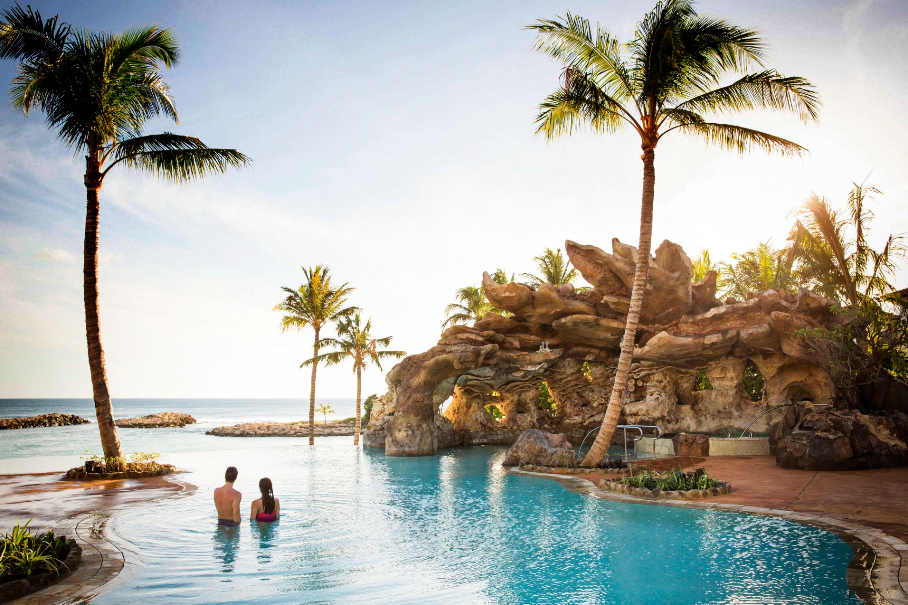 Couple relaxing in the Ka Maka infinity pool at Aulani, A Disney Resort & Spa overlooking the Pacific Ocean at sunset
